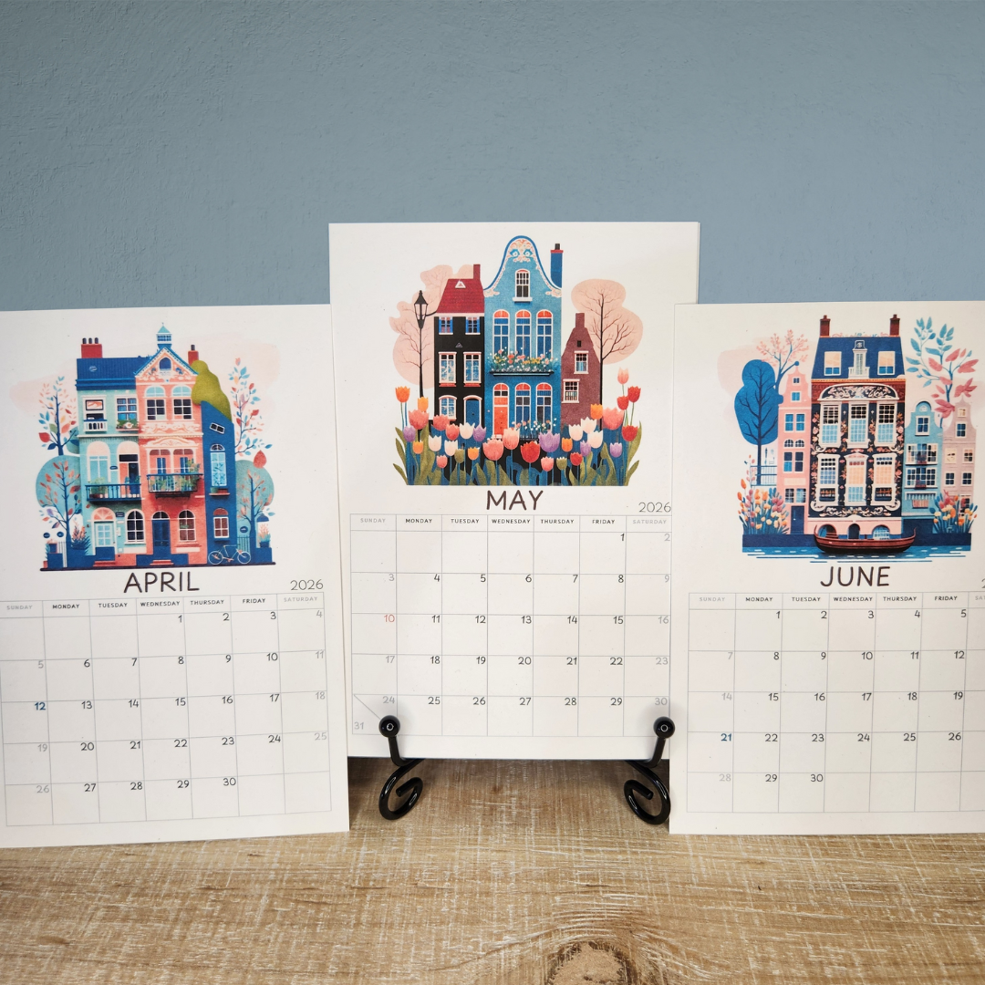 Three calendar pages showing April, May, and June with illustrated houses and flowers on a wooden surface.