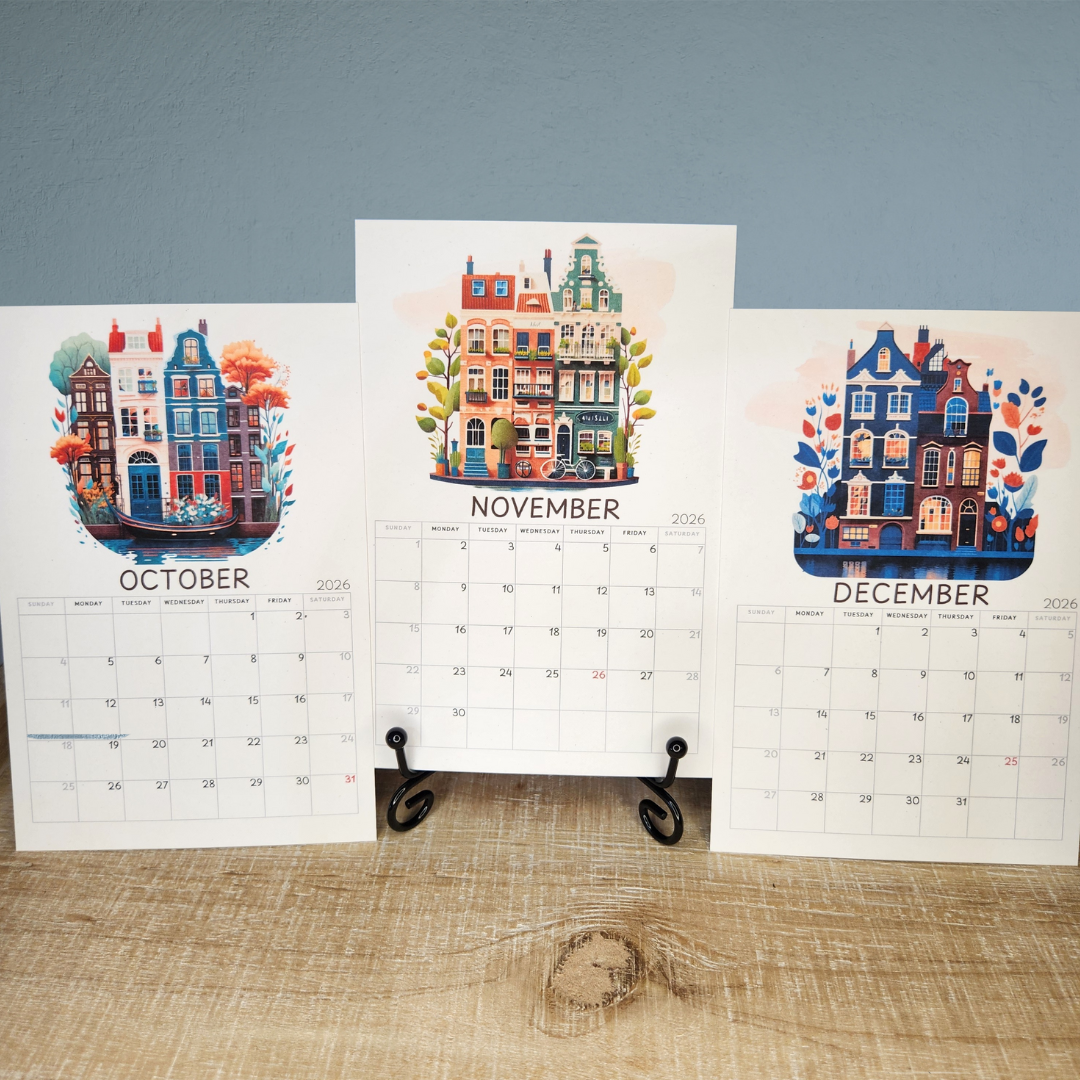 Three calendar pages for October, November, and December with illustrated buildings on a wooden surface.