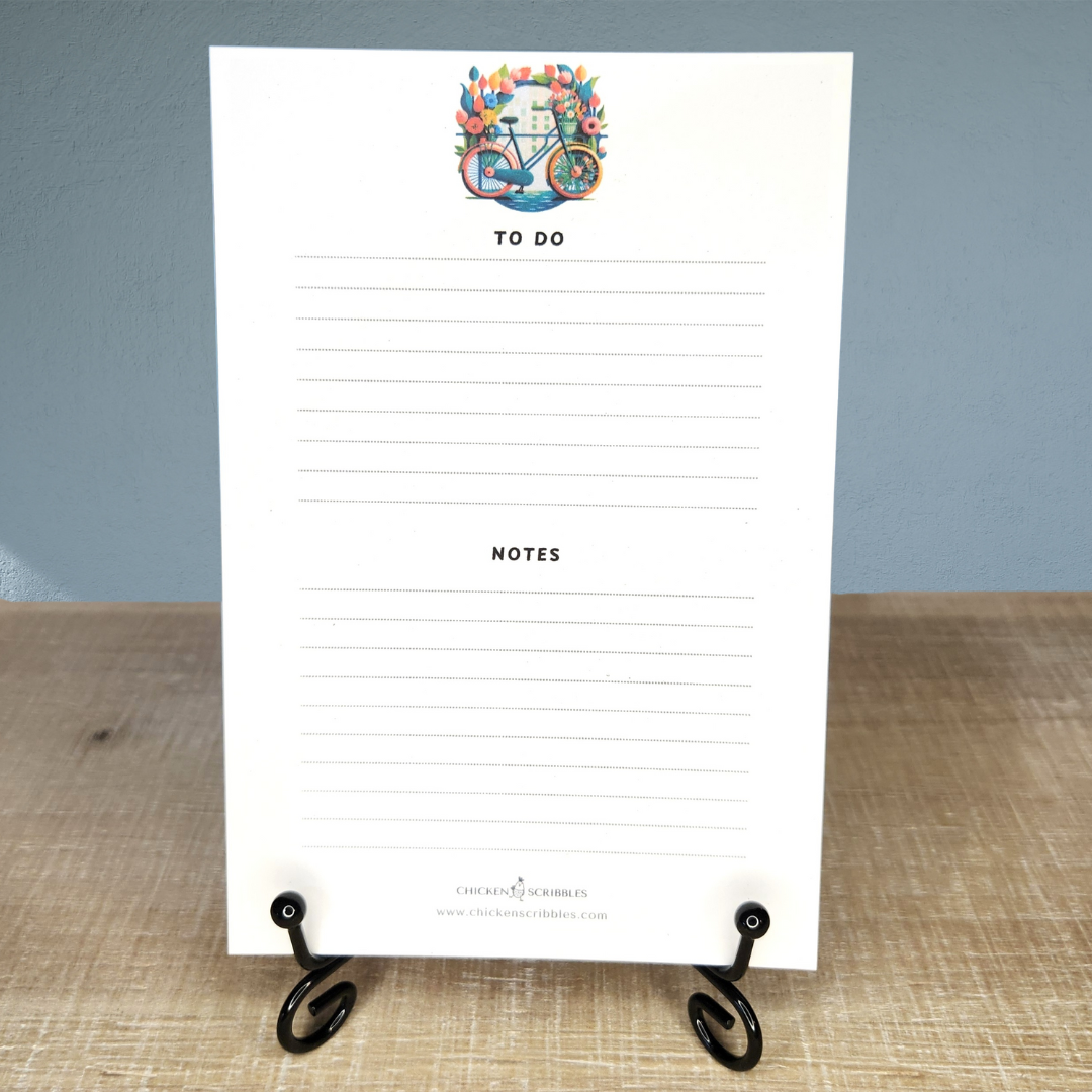 White notepad with decorative bicycle design and text on a wooden surface.