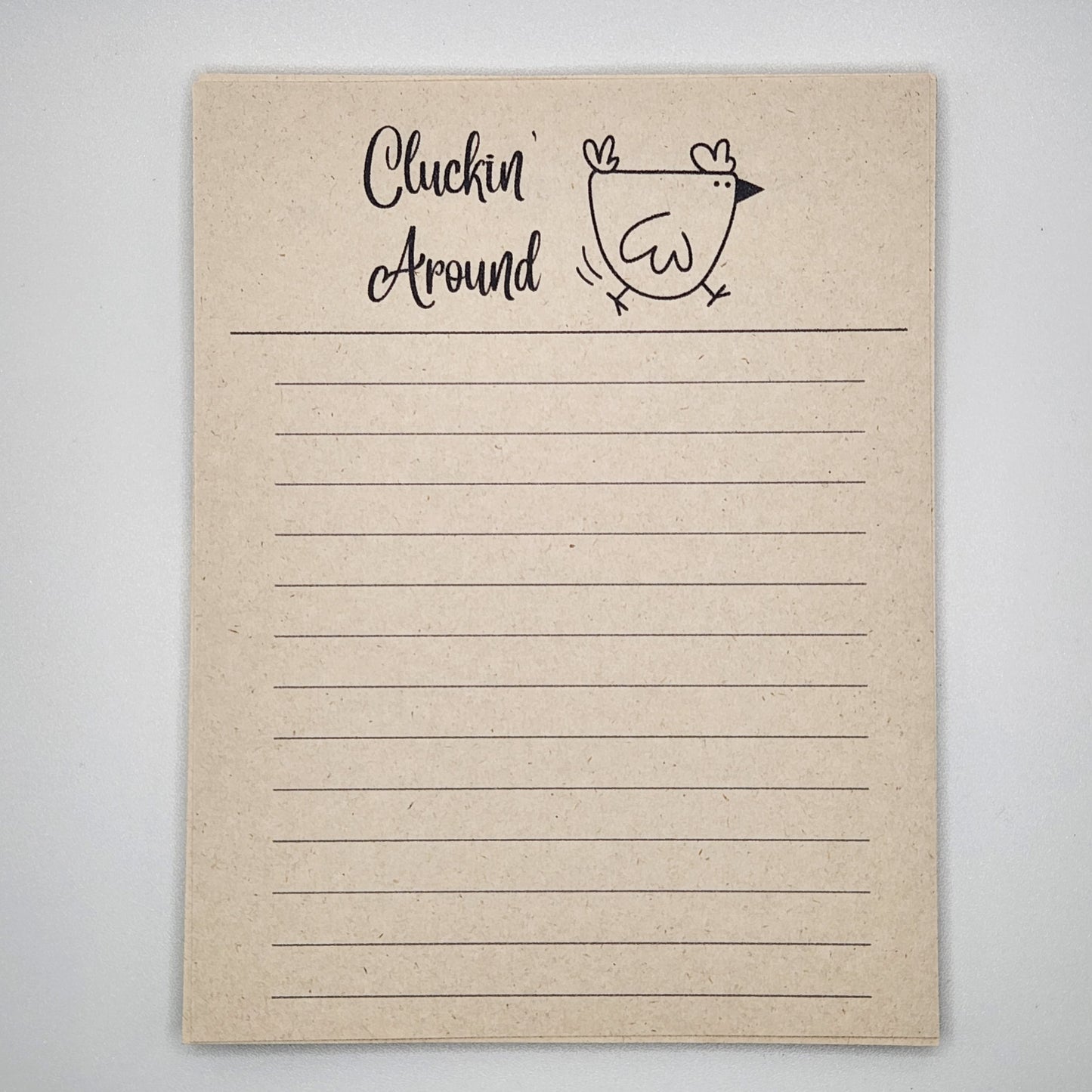 Natural sugarcane notepad on white background. Cartoon chicken at the top is running to the left and the words Cluckin' Around is written to the left of the chick.  Lines fill the remainder of the page.