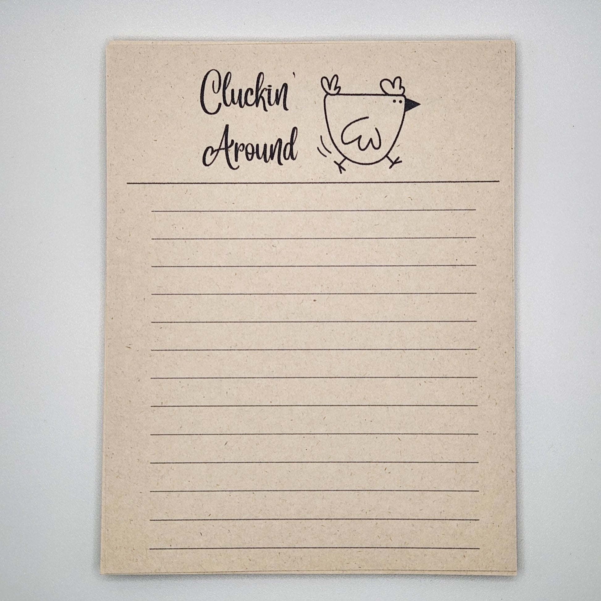 Natural sugarcane notepad on white background. Cartoon chicken at the top is running to the left and the words Cluckin' Around is written to the left of the chick.  Lines fill the remainder of the page.