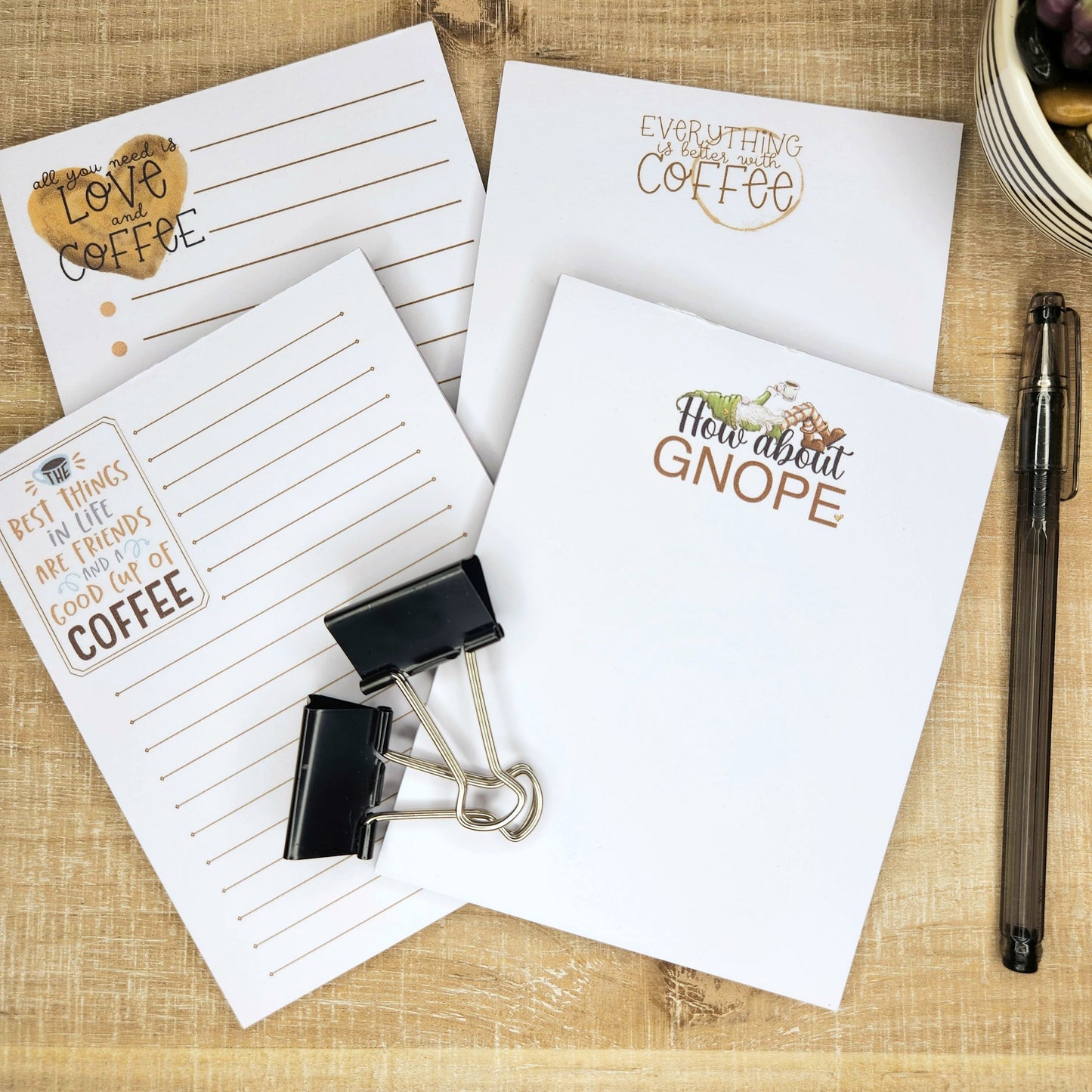 4 coffee related notepads are placed on a wooden background.  Each notepads has a different saying about coffee.