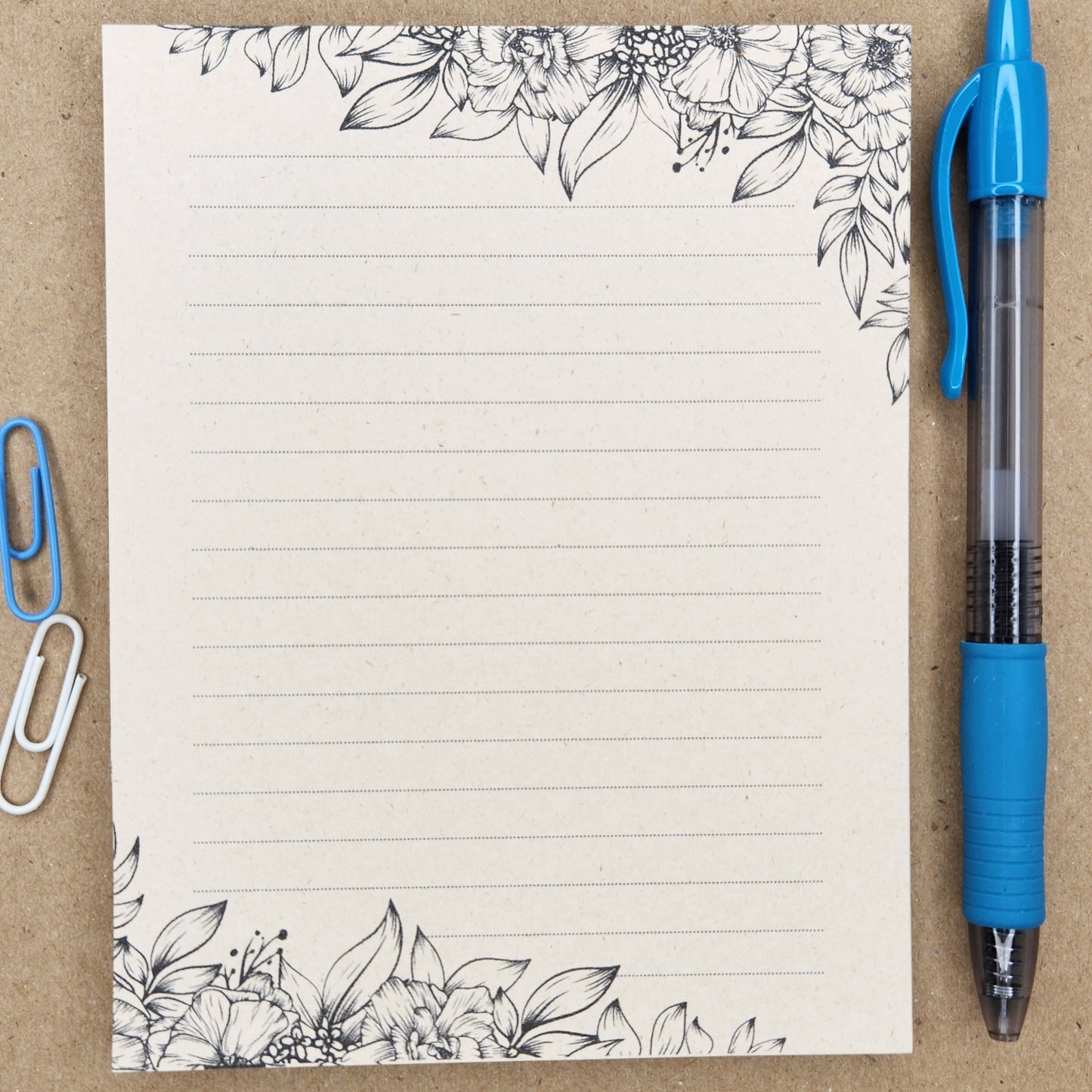 Soft beige sugarcane notepad on a tan background. Note pad is lined and is accented by various flowers and foliage on the top and bottom corners.
