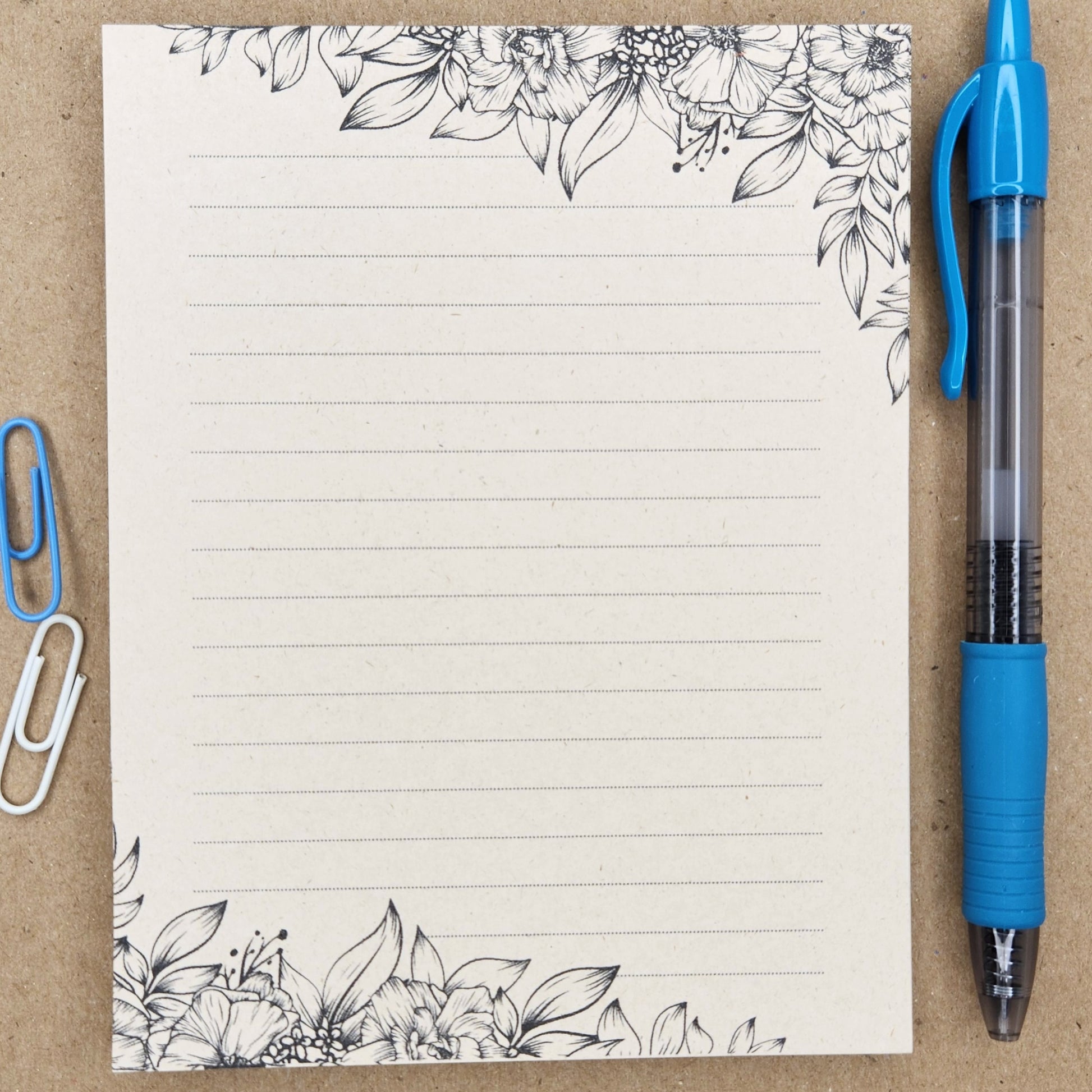 Soft beige sugarcane notepad on a tan background. Note pad is lined and is accented by various flowers and foliage on the top and bottom corners.