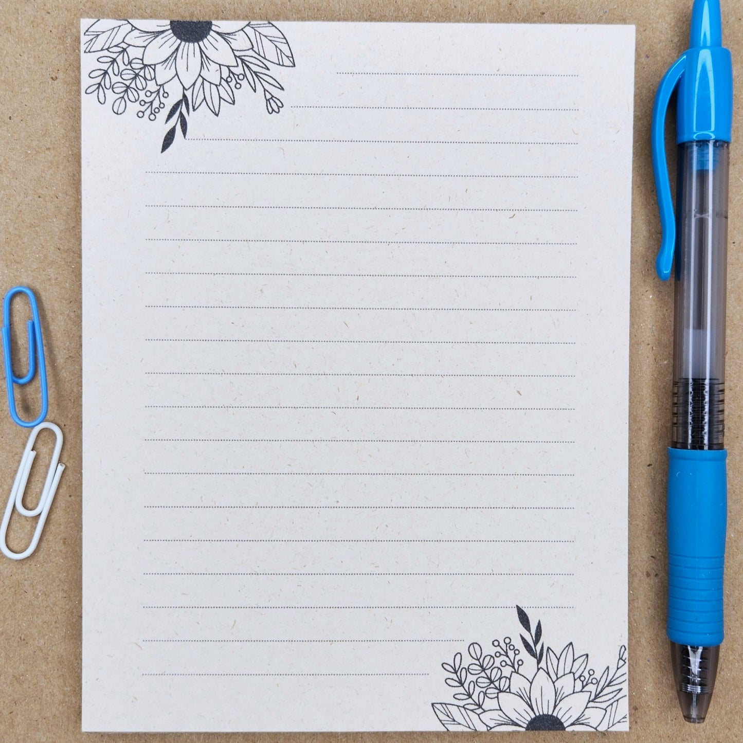 Soft beige sugarcane notepad on a tan background. Note pad is lined and is accented by flowers on the top and bottom corners.
