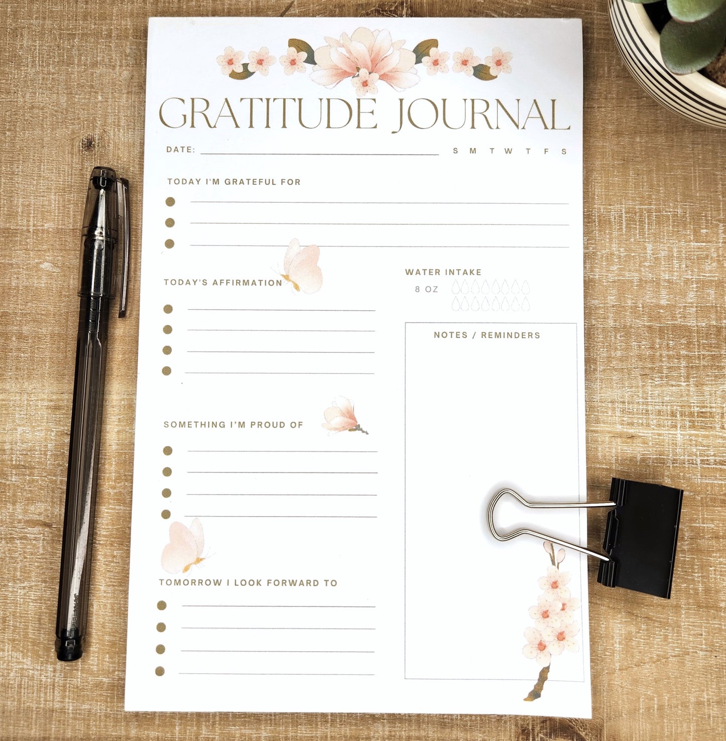 Beautiful half page gratitude journal printed on white paper and laying on a wooden background. Words on the page: gratitude Journal, date, today i'm grateful for, Today's affirmations, something I'm proud of, tomorrow I look forward to , water intake, notes/reminders.