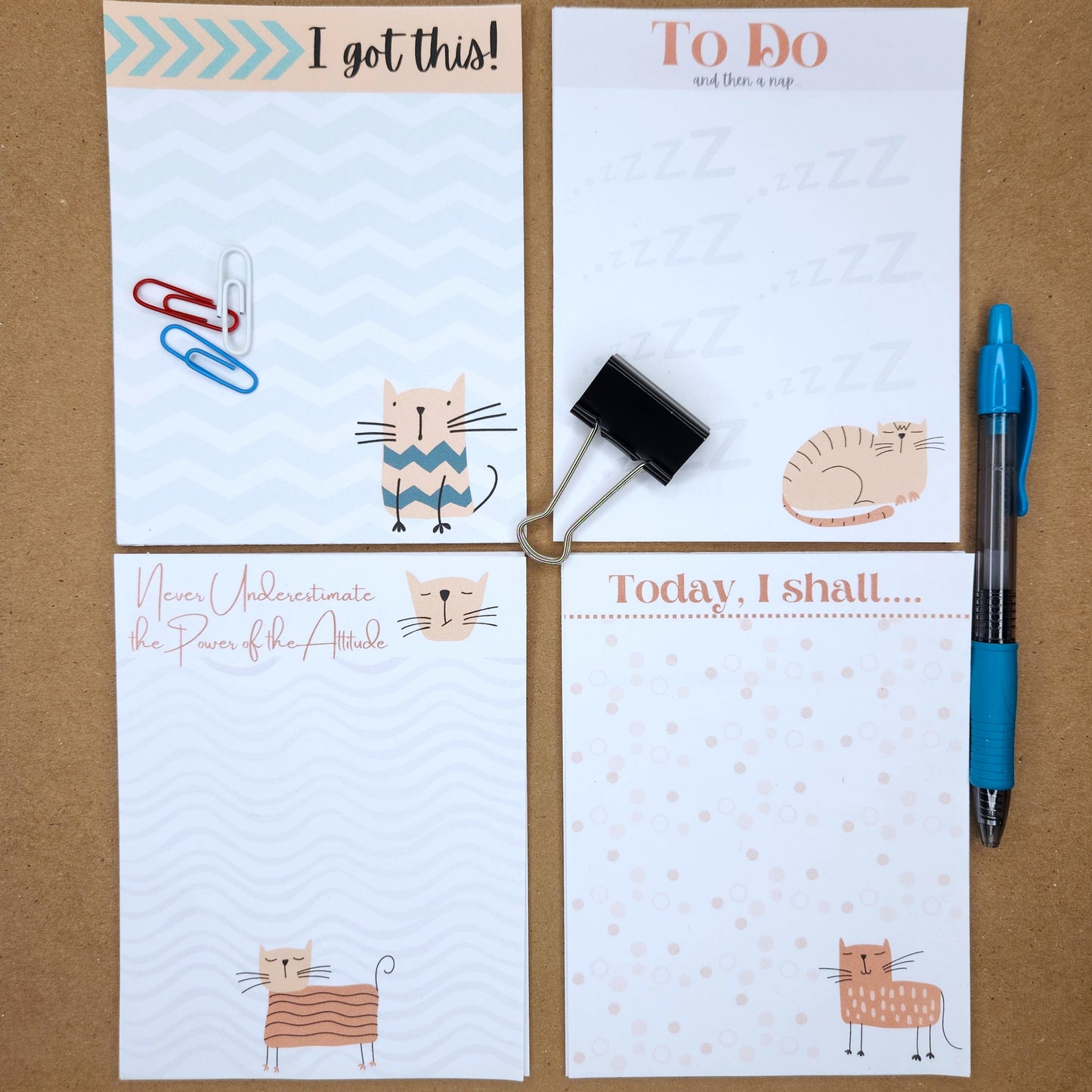 Set of  four white notepads on a tan background.  Each notepad has a cartoon cat with a different saying.