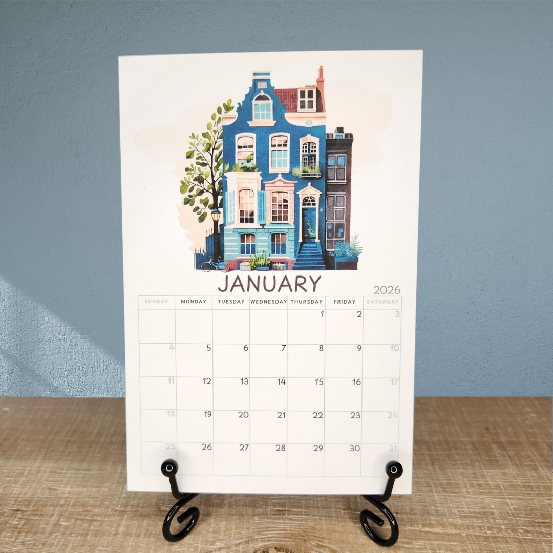 Calendar for January 2026 with colorful house illustration on a stand against a blue wall.