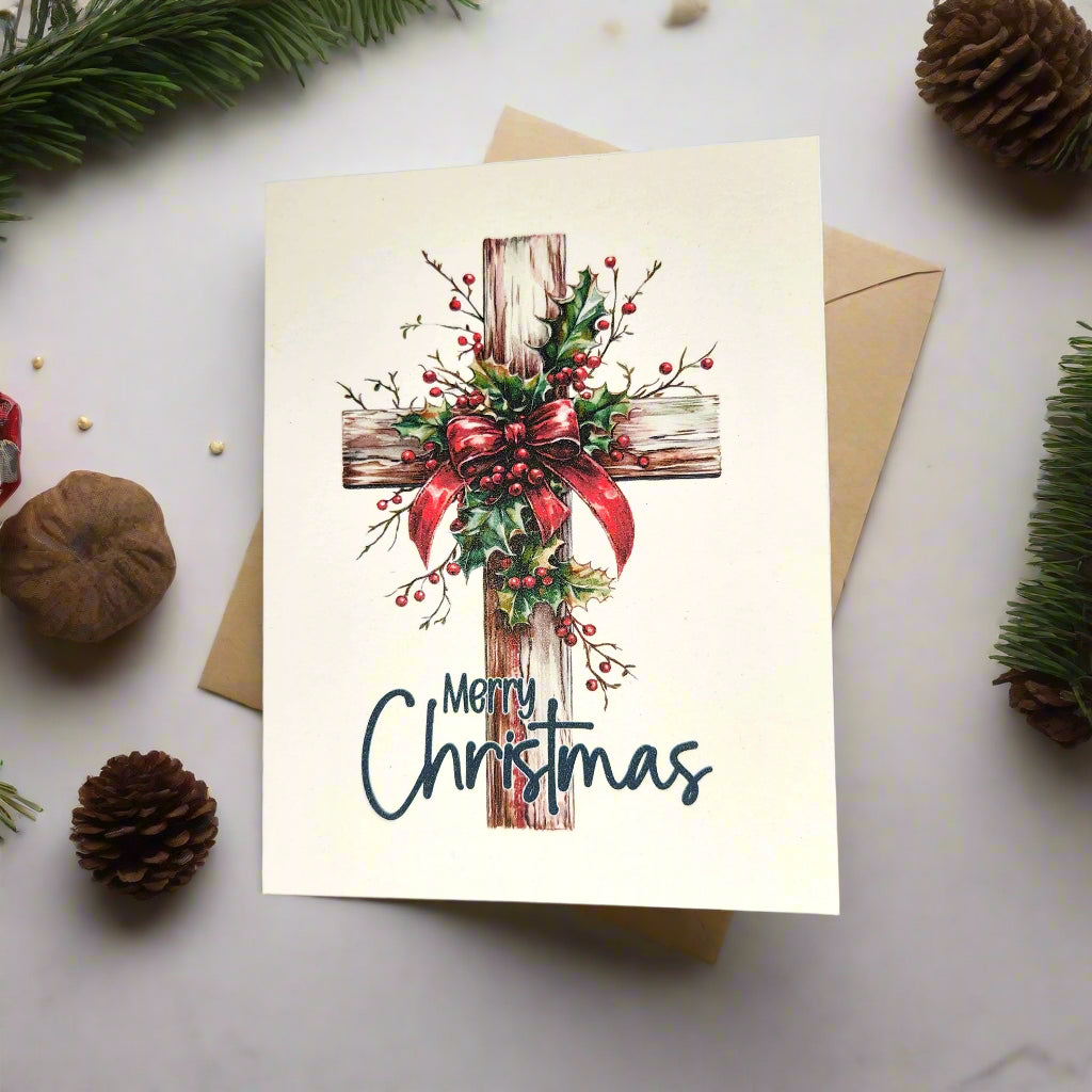 Christmas card with a cross and holly design on a white surface with pine cones and branches.