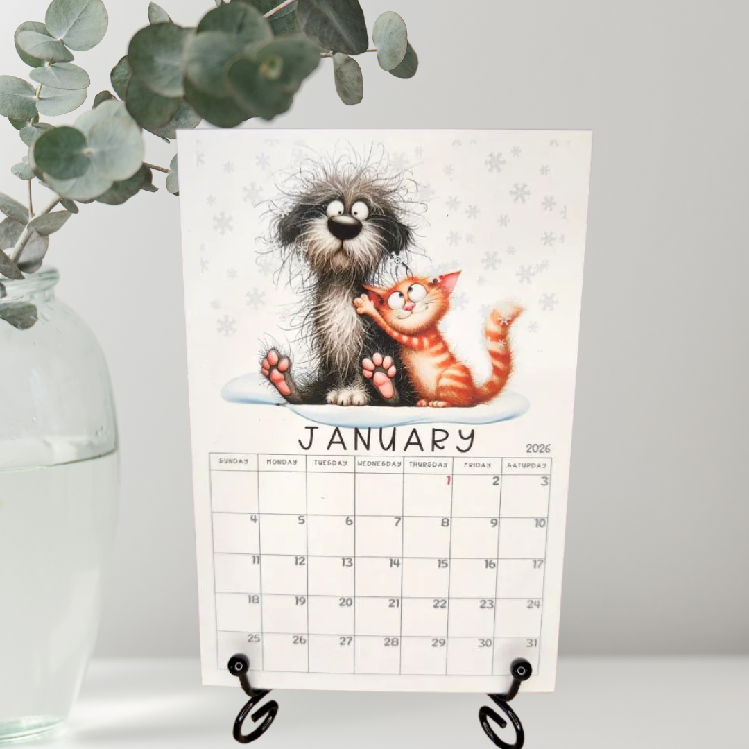 Calendar with a cartoon dog and cat illustration for January on an easel, with a plant in the background.