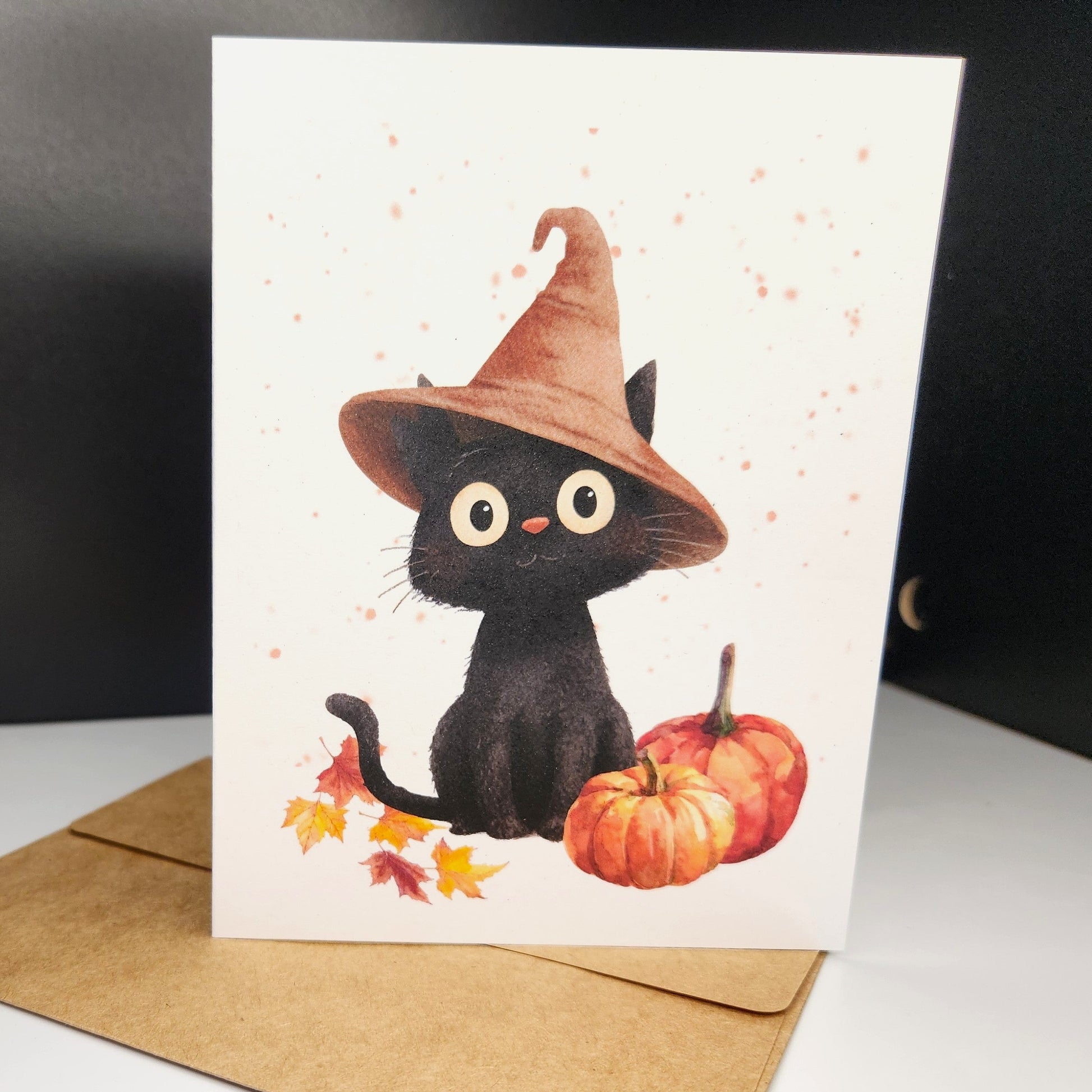 black kitten in tan hat with pumpkin and leaves surrounding it.  All this cuteness on a greeting card