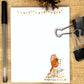 Notepad with a snowman illustration and 'Merry & Bright' text, pen, and clips on a wooden surface.