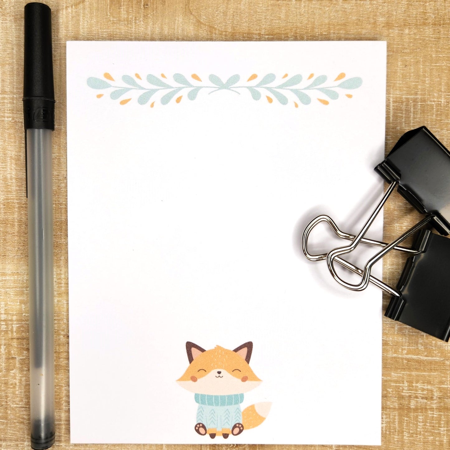 cute orange fox dressed in a blue sweater sits at the bottom middle of each page of this 50count notepad.  The top of the page is adorned with a minimal floral design in coordinating colors. 