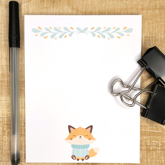 cute orange fox dressed in a blue sweater sits at the bottom middle of each page of this 50count notepad.  The top of the page is adorned with a minimal floral design in coordinating colors. 