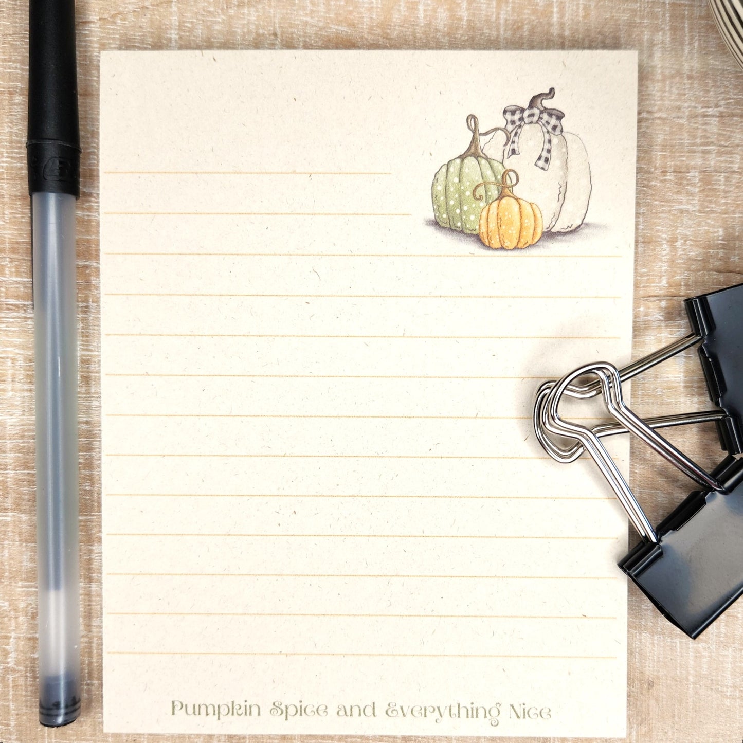 Beige colored sugarcane notepad on white barnboard background. Lined notepad has white, green and orange pumpkin at the top with the words Pumpkin spice and everything nice at the bottom.