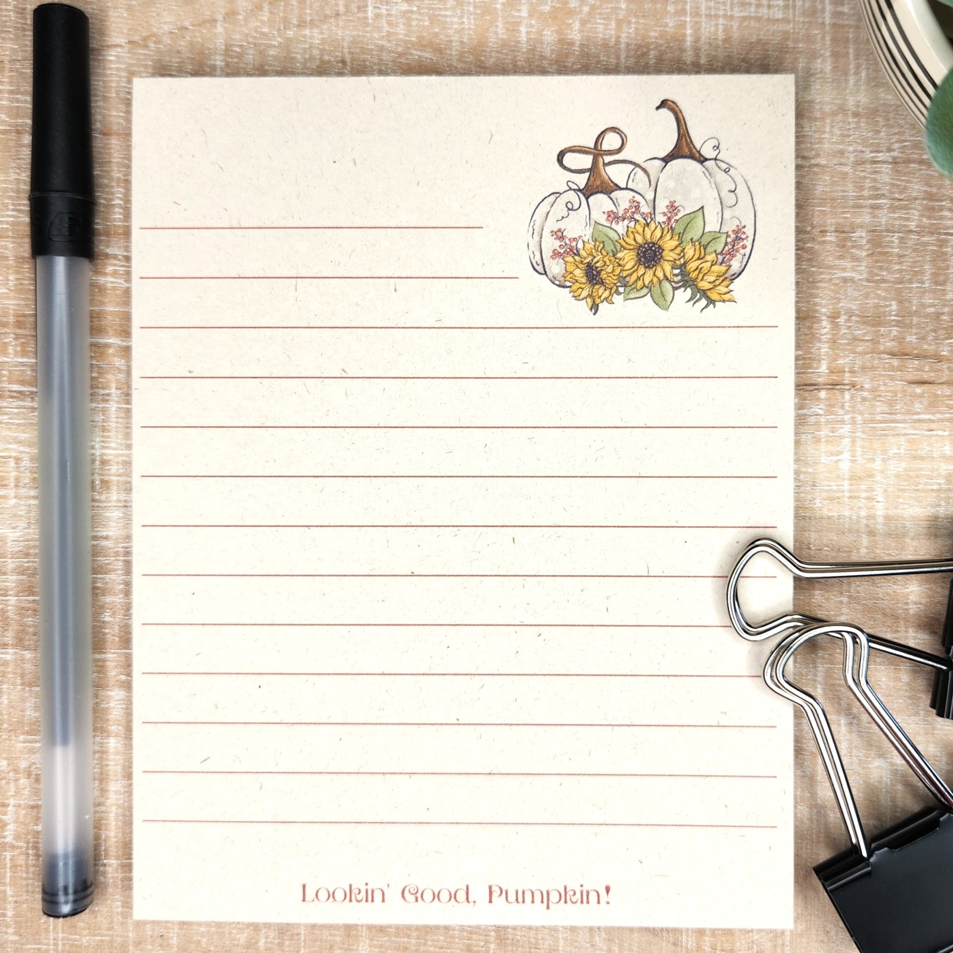 Beige colored sugarcane notepad on white barnboard background. Lined notepad has two white pumpkins with sunflower accents and the words "Lookin' good, Pumpkin!" on the bottom center of the page