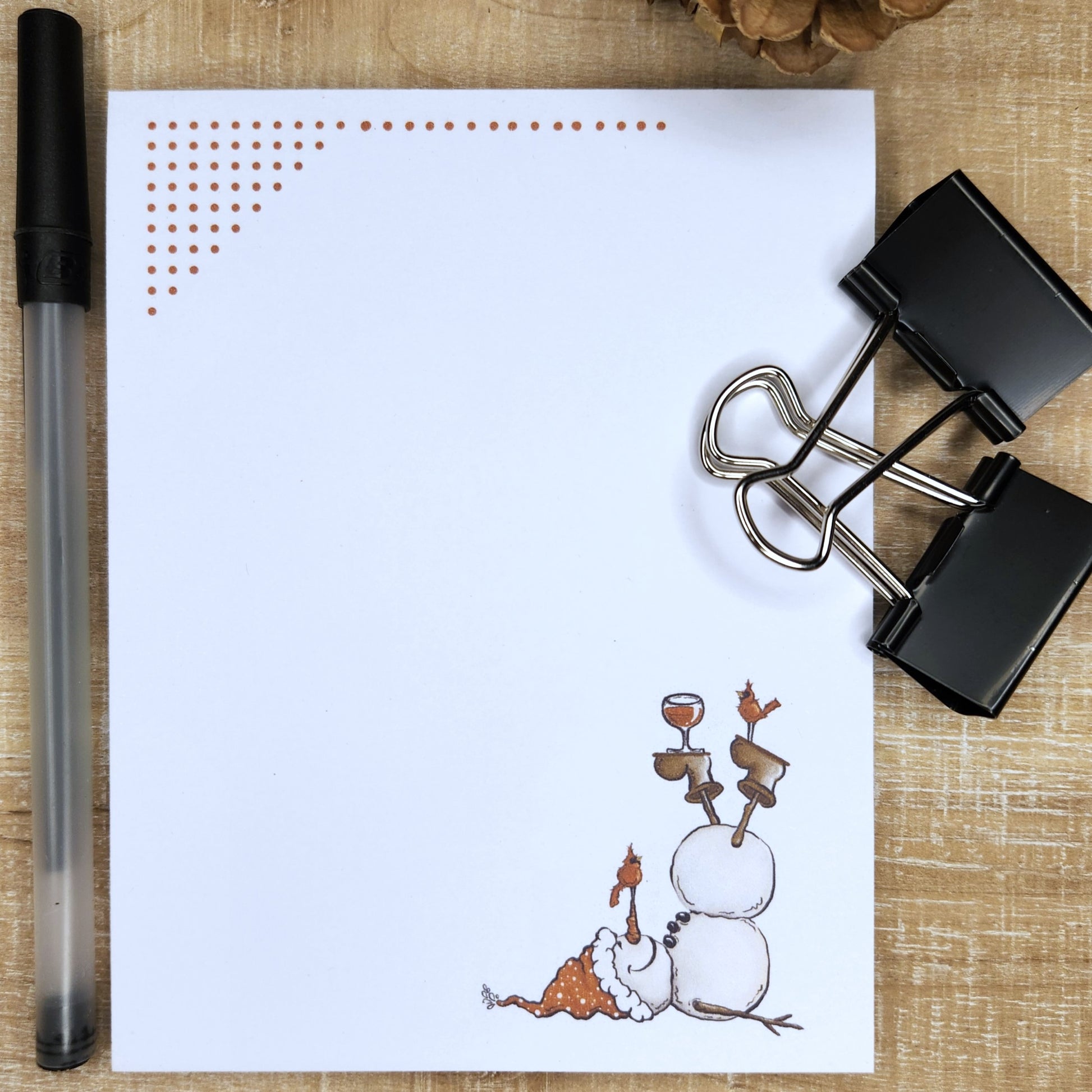 white notepad on tan and red background. red dots accent the top of the page. snowman with wine glass is laying on the bottom right corner of the page.