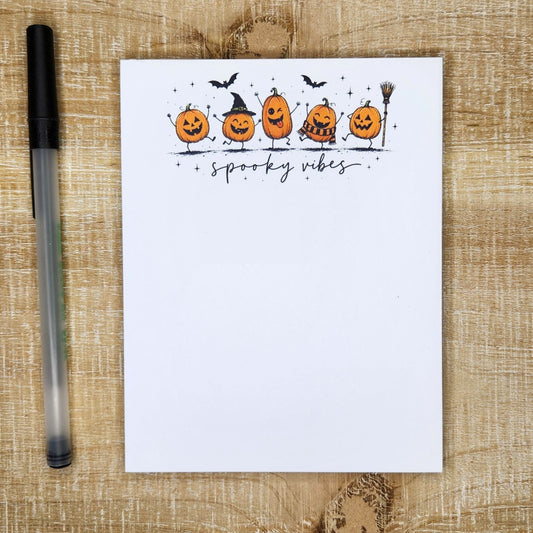 dancing pumpkins line the top of the notepad. Words "Spooky Vibes" in cursive is under the pumpkins