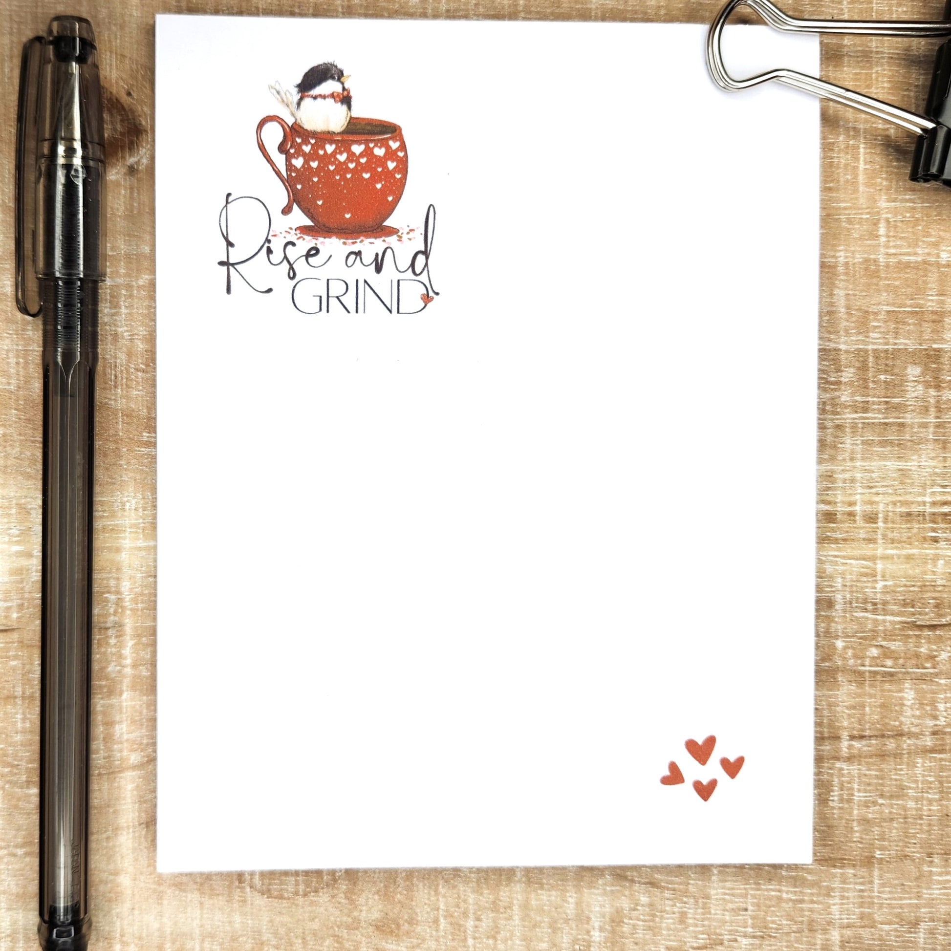 Rise and grind written on the top left corner of the notepad. Image is of a little bird sitting in a red cup with white hearts . Bottom right corner of the page has an image of 4 little hearts. 