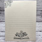 Soft beige sugarcane paper notepad on white barn board background.  Note pad is lined and has flower accent on the upper left corner and open book with flowers coming out of the center on the bottom center of the page. all designs are line drawings. 