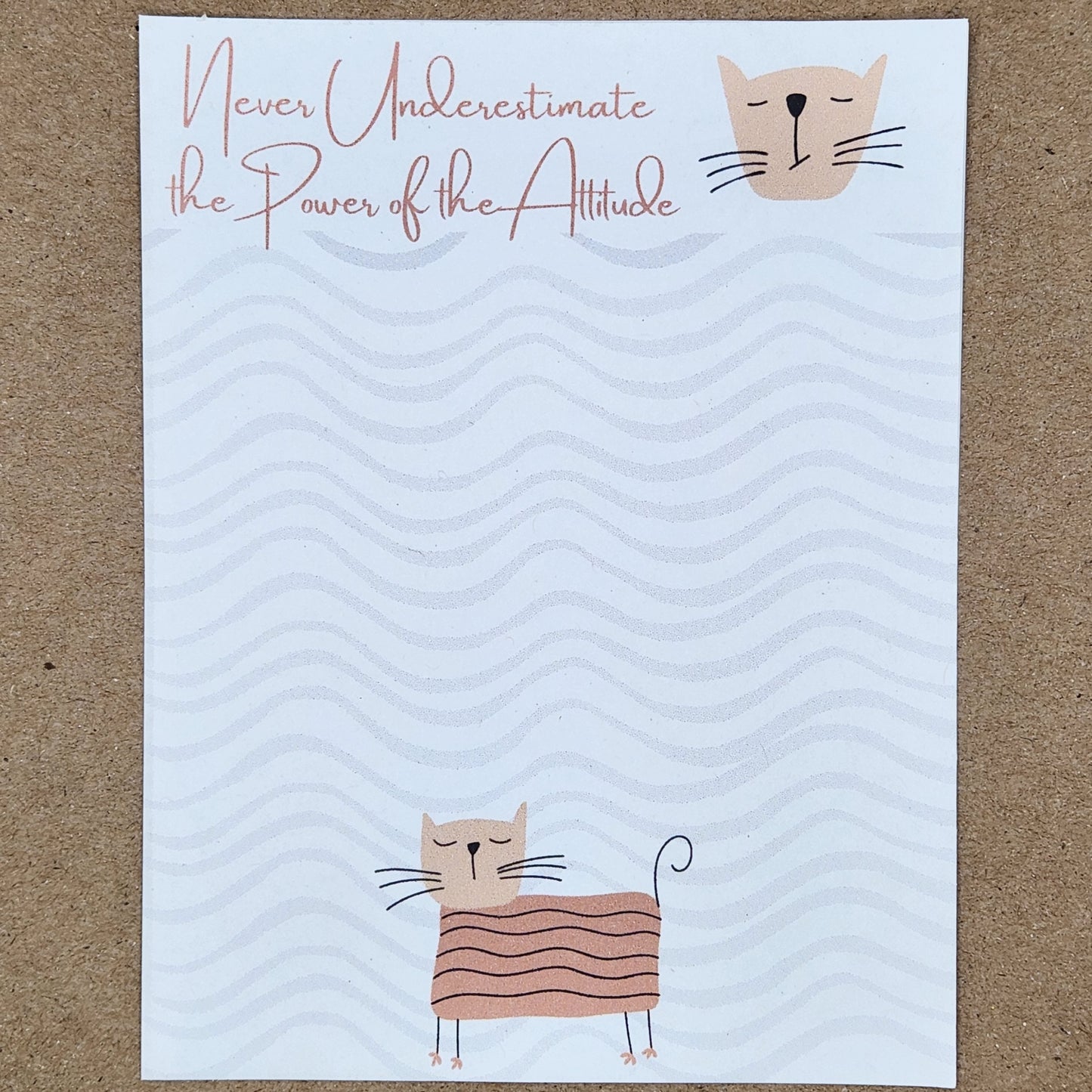 white notepad on tan background. Cat in the center bottom of the page. wave design throughout the page. Top is accented by a blush border with the words 'Never underestimate the power of the attitude"