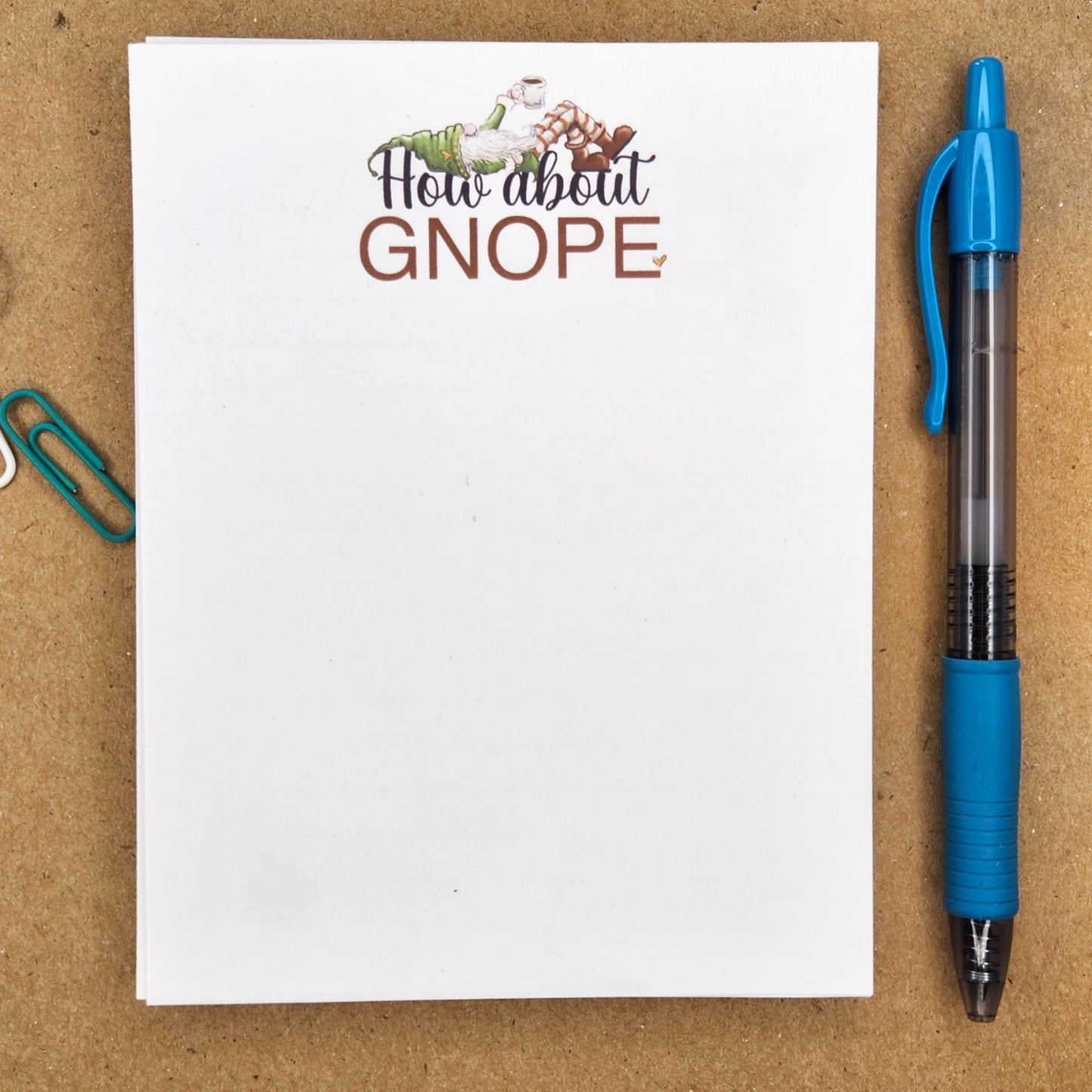 Notepad is laying on a tan background.  in the top center of the notepad is a gnome holding a cup of coffee and laying on the words "how about GNOPE'  