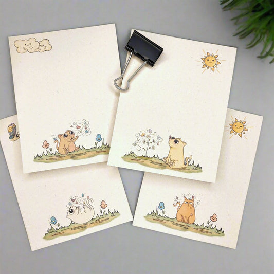 4 natural sugarcane notepads on a tan background. Each notepad depicts a cartoon kitty with butterflies and flowers.