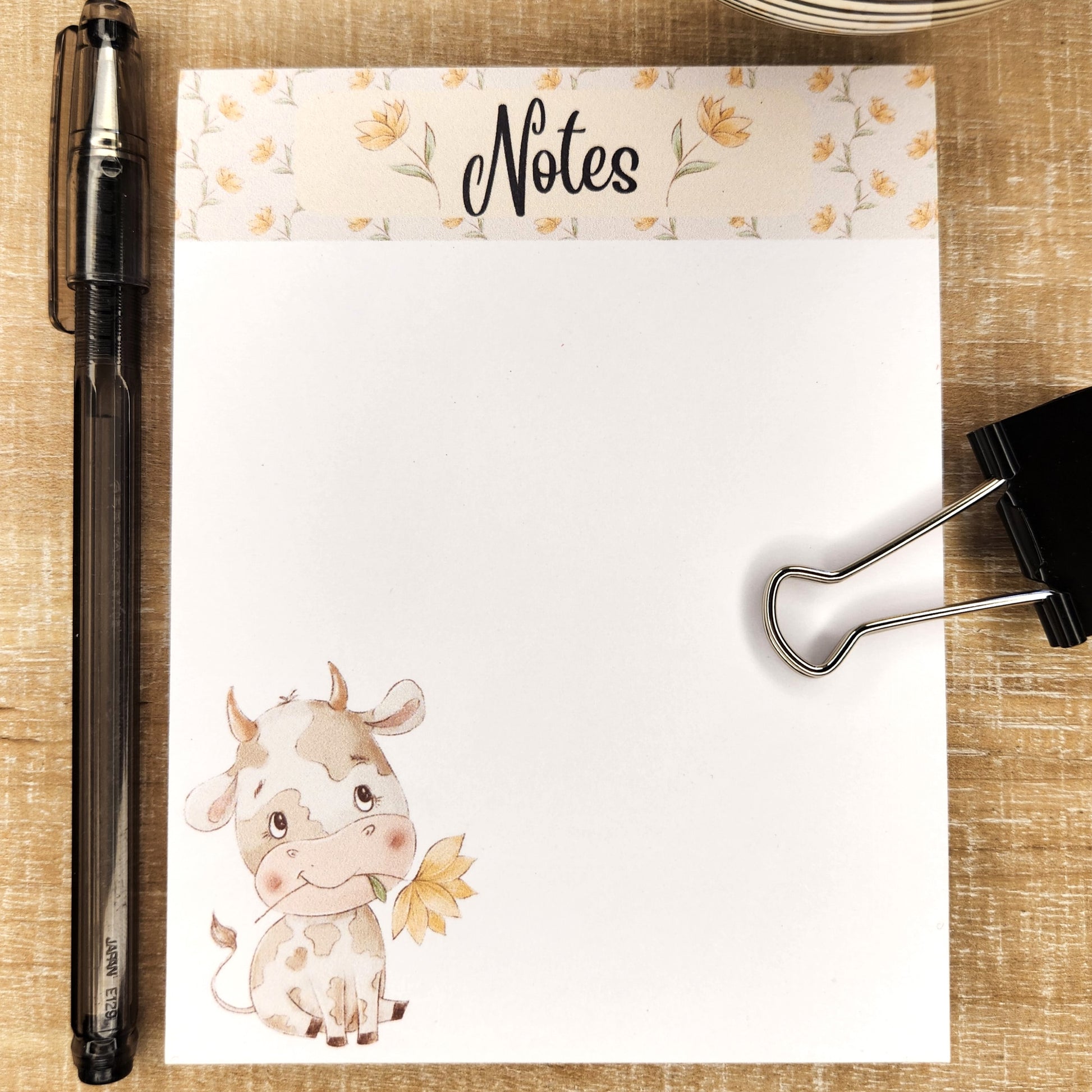 White notepad on blue background. a floral border runs along the top inch of the page with the word Notes in the center. The lower right bottom corner show a cartoon cow sitting holding a flower in it's mouth.