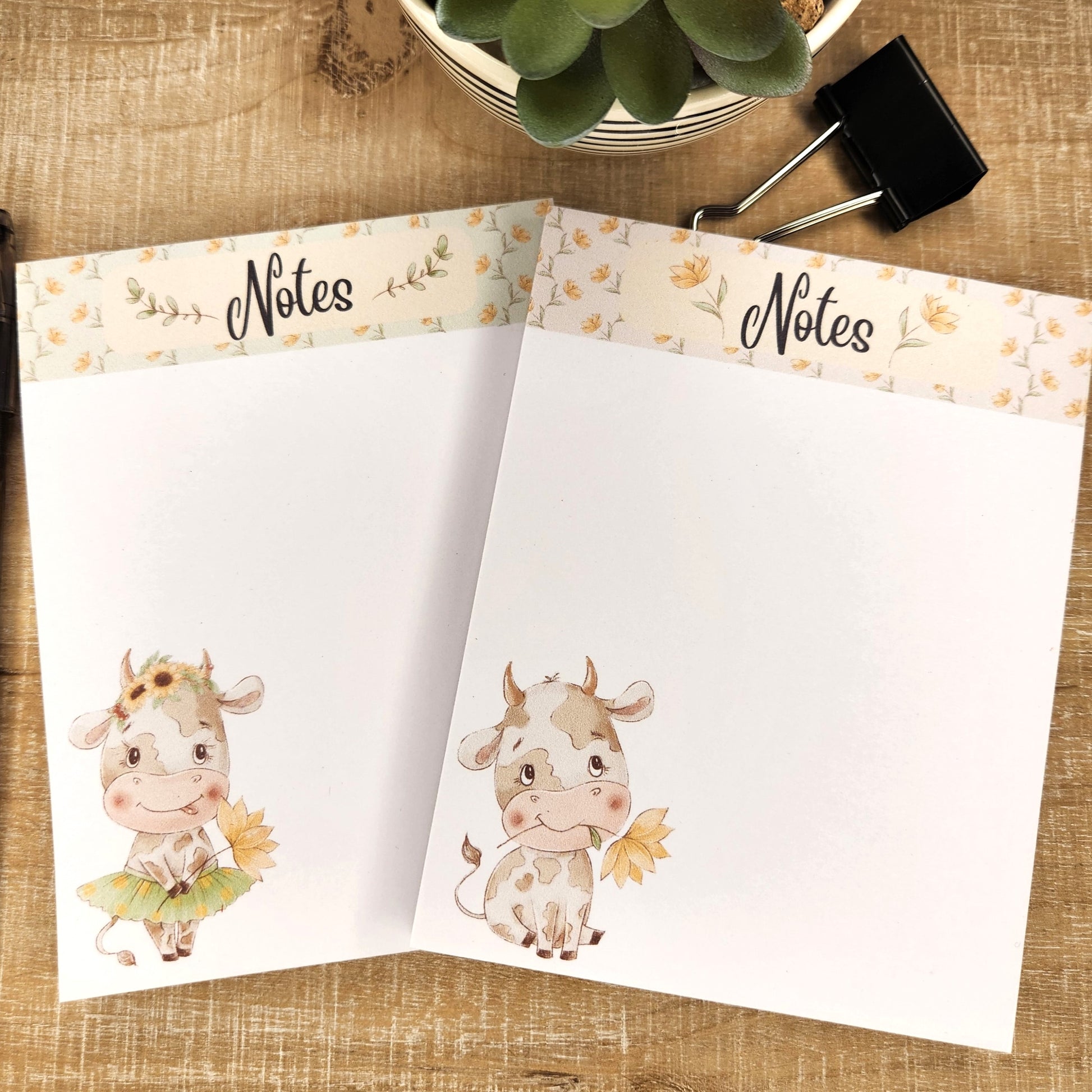 Two white notepads on a tan background. Each notepad has a floral top band with the word Notes at the top. the lower right hand corner shows a cow with flowers.