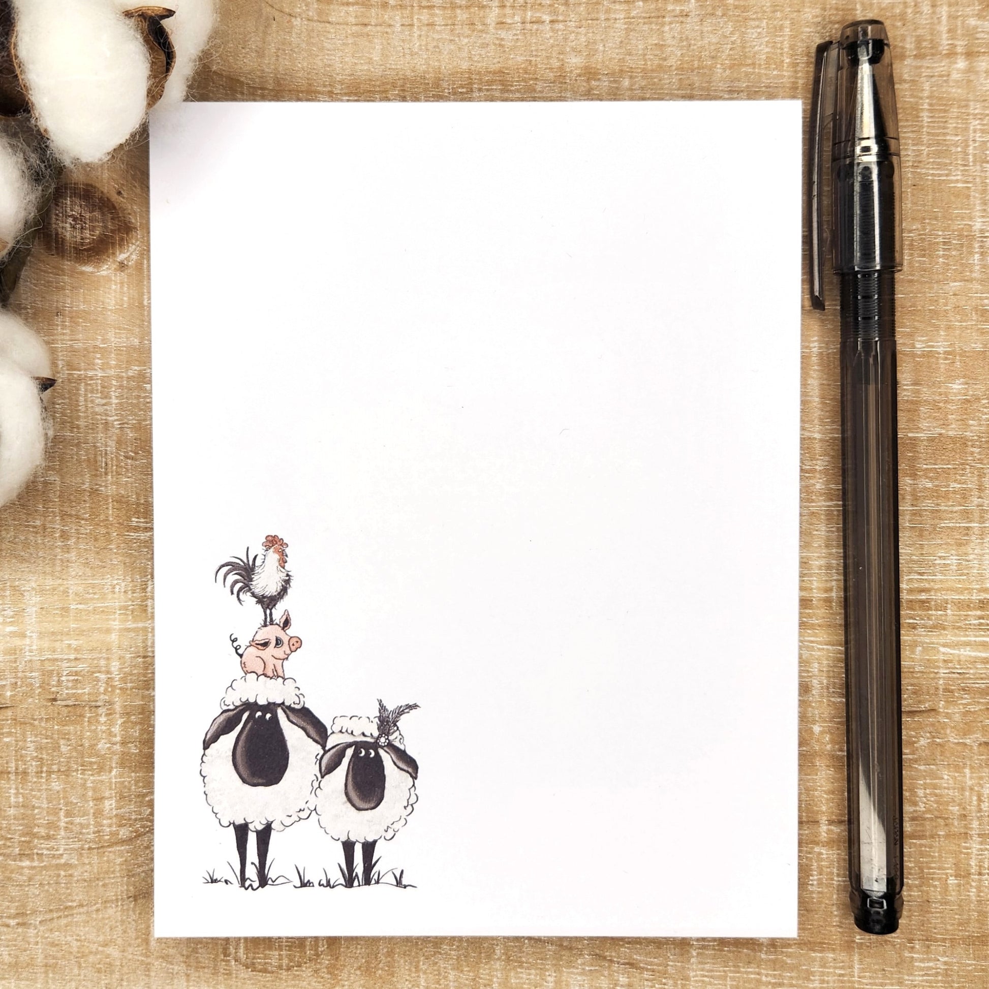 Notepad depicts two sheep.  One sheep has a pig on its head and a rooster on the pigs' head.  design is in the lower left corner of the page. 