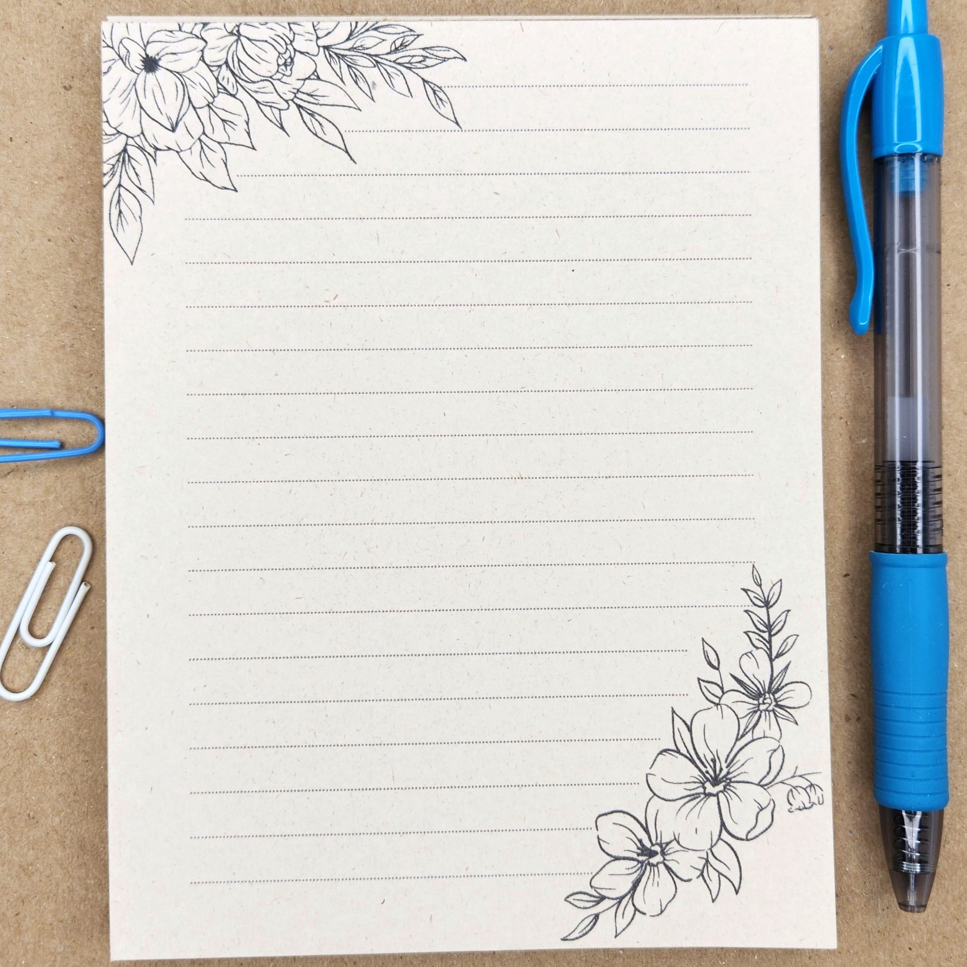 Soft beige sugarcane notepad on a tan background. Note pad is lined and is accented by flowers on the top and bottom corners.