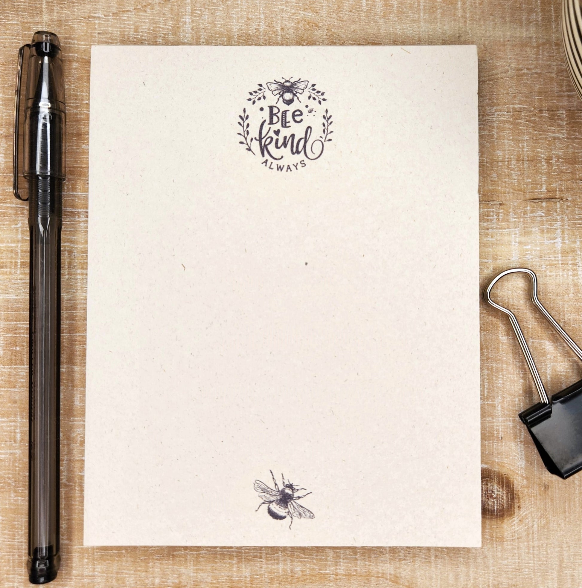 tan sugarcane paper notebook is in front of a white barn board background. the image of a bee and flowers enhance the words 'bee kind always'. a small bee in show on the bottom center.