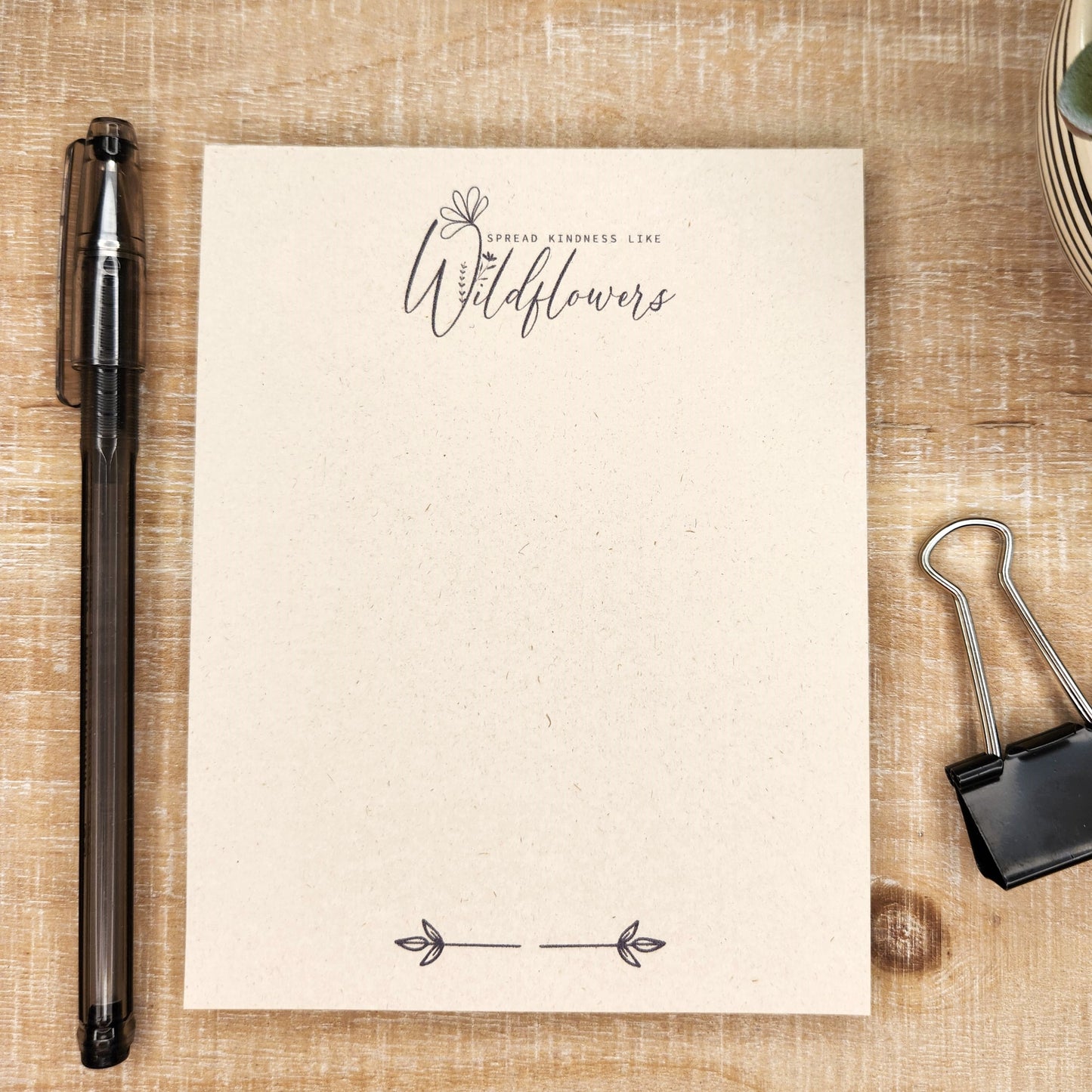 tan sugarcane paper notepad on white barn board background. the words ' spread kindness like wildflowers' in at the center top of the page and small leaf accent in on the bottom center.