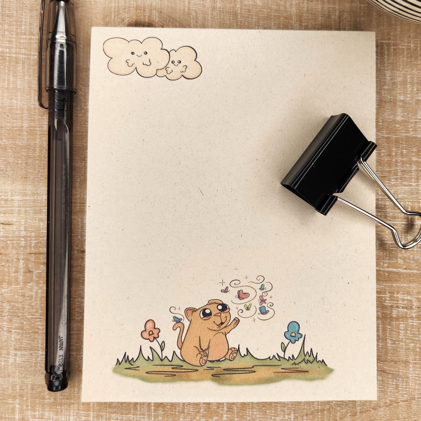 Natural sugarcane notepad on white background. Notepad depicts clouds in the upper left hand corner and sweet cartoon kitty with a butterfly flying around it sitting on a patch of grass.