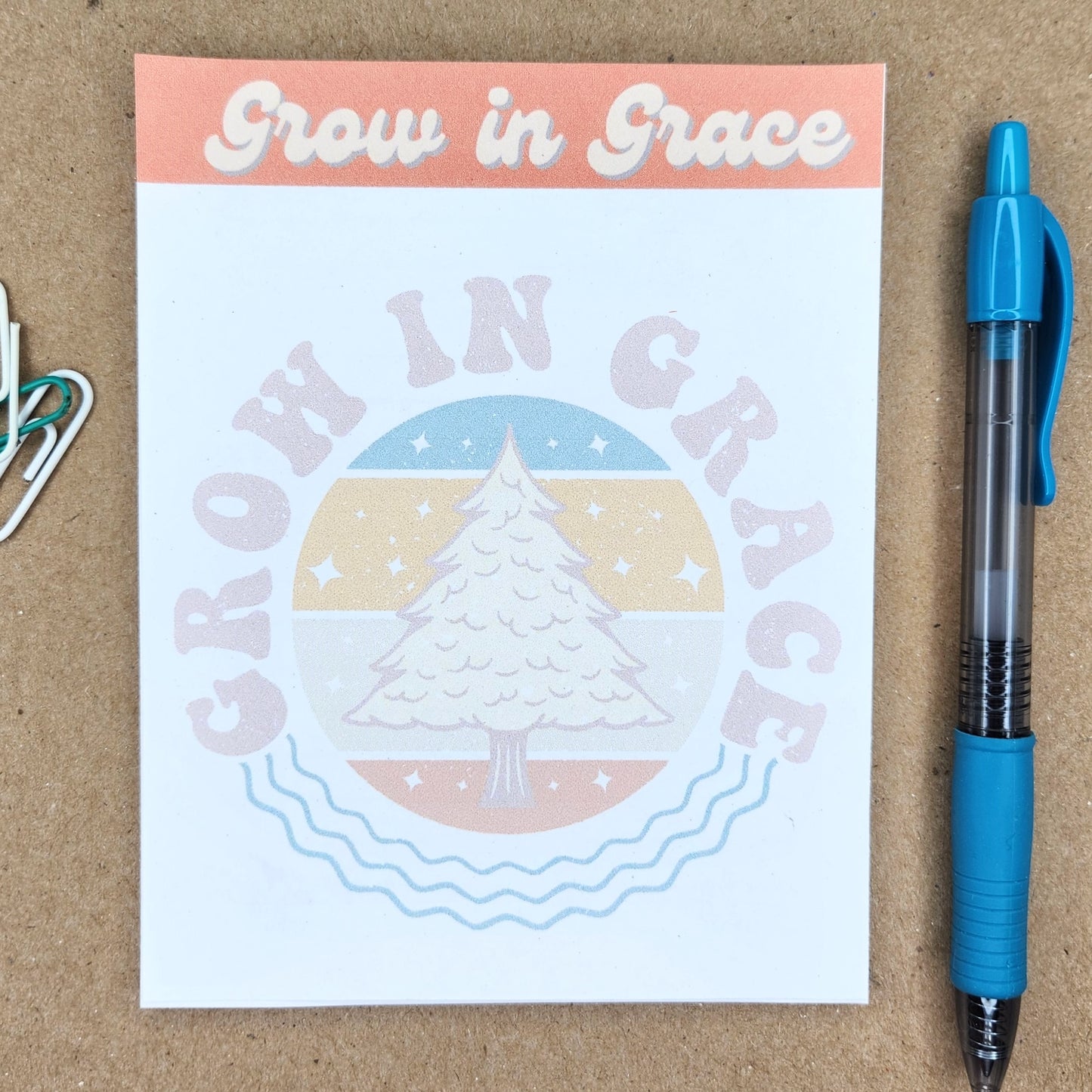 White notepad on a tan background. Words grow in grace in a retro style. Center of notepad has a tree with the words Grow in Grace