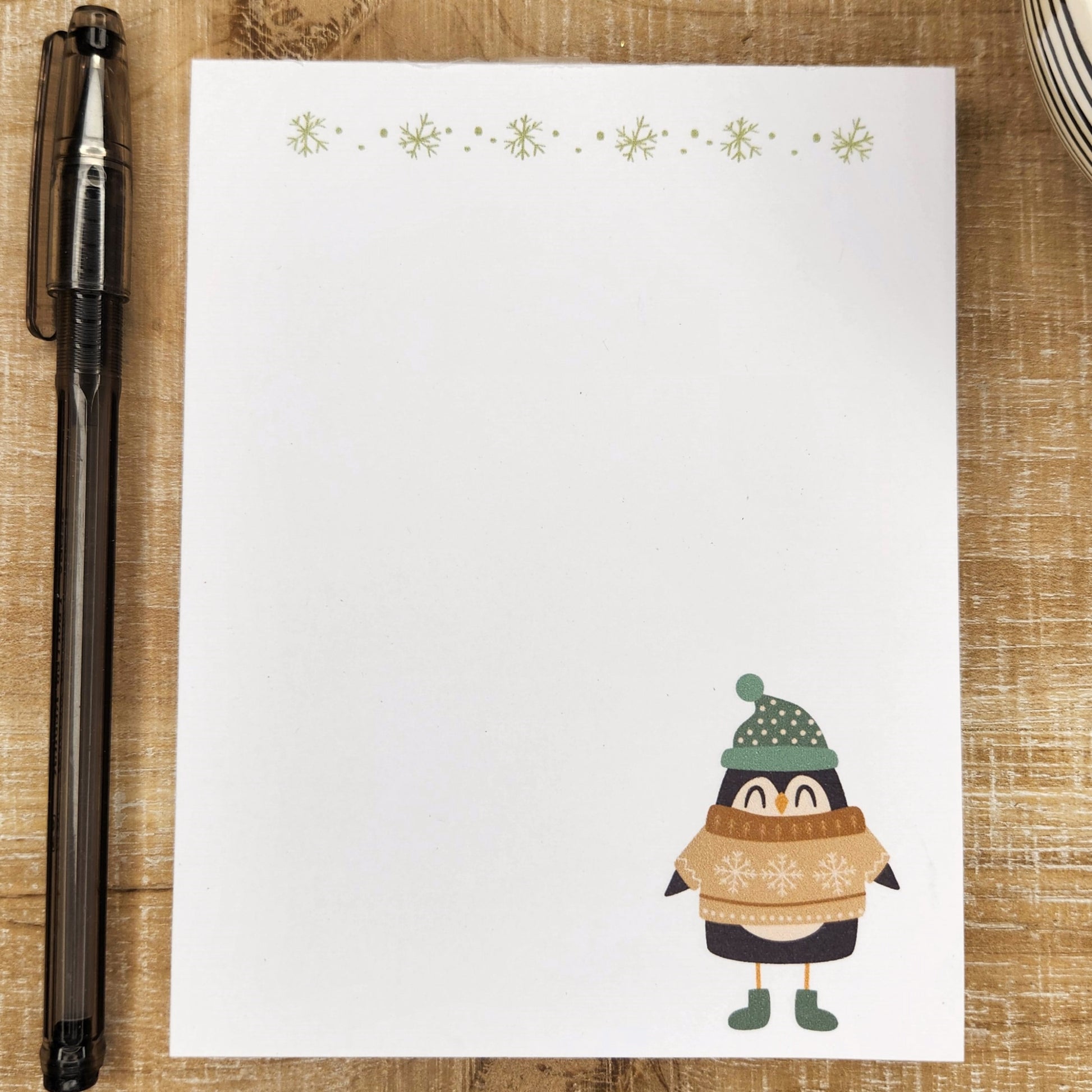 Penguin wearing a sweater and boots and hat are on the right corner of the notepad.  Green snowflakes that match the sweater line the top of the page.