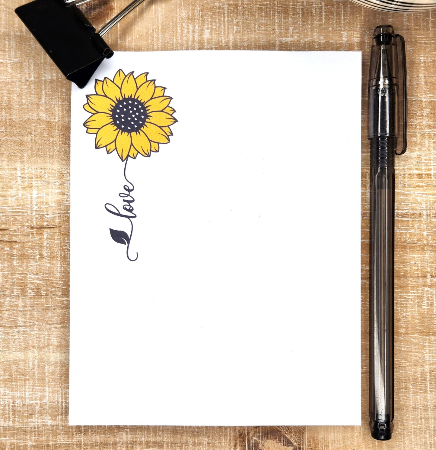 white notepad with a sunflower and a word trailing as the stem.  Word is love.