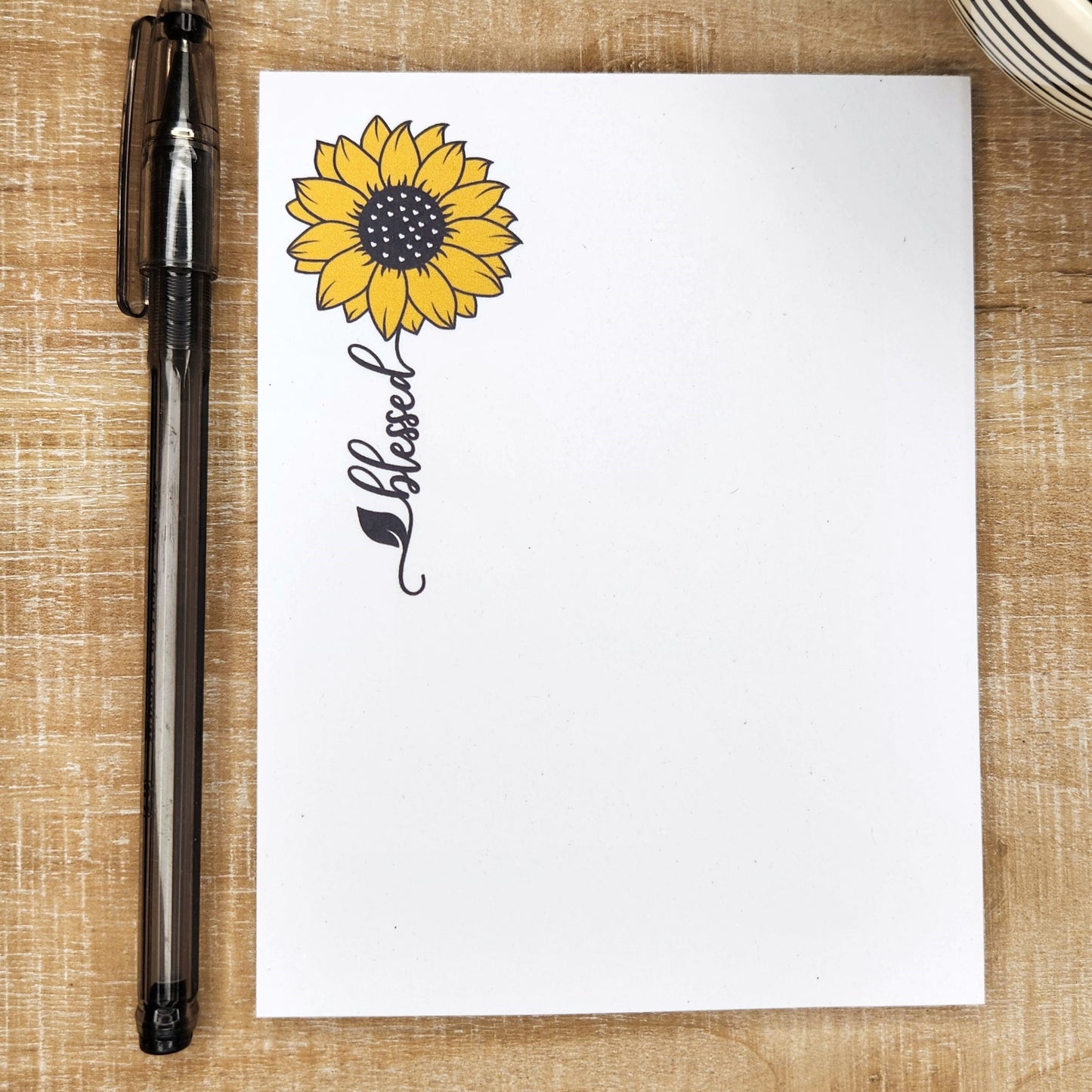 white notepad with a sunflower and a word trailing as the stem. Word is blessed