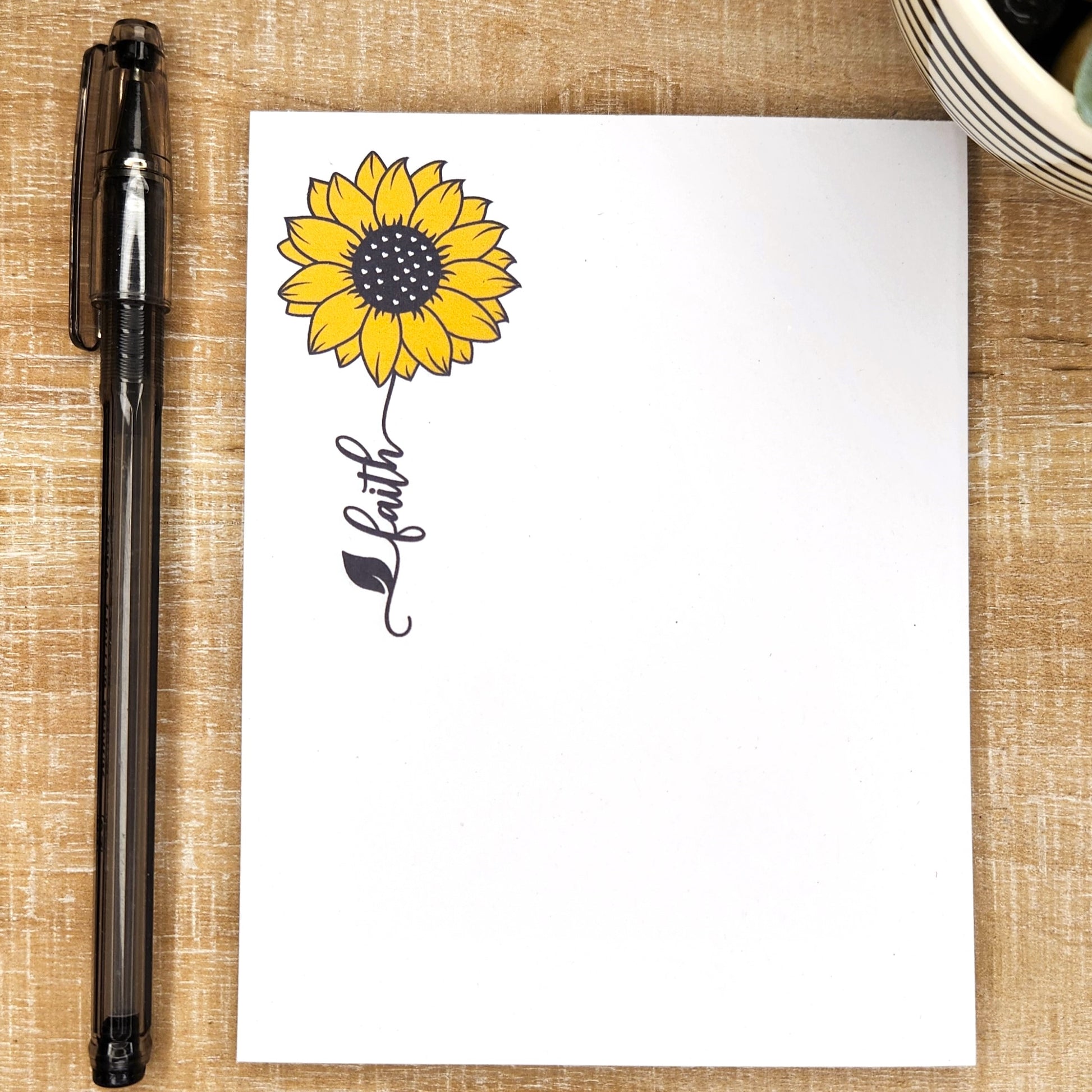 white notepad with a sunflower and a word trailing as the stem. Word is faith