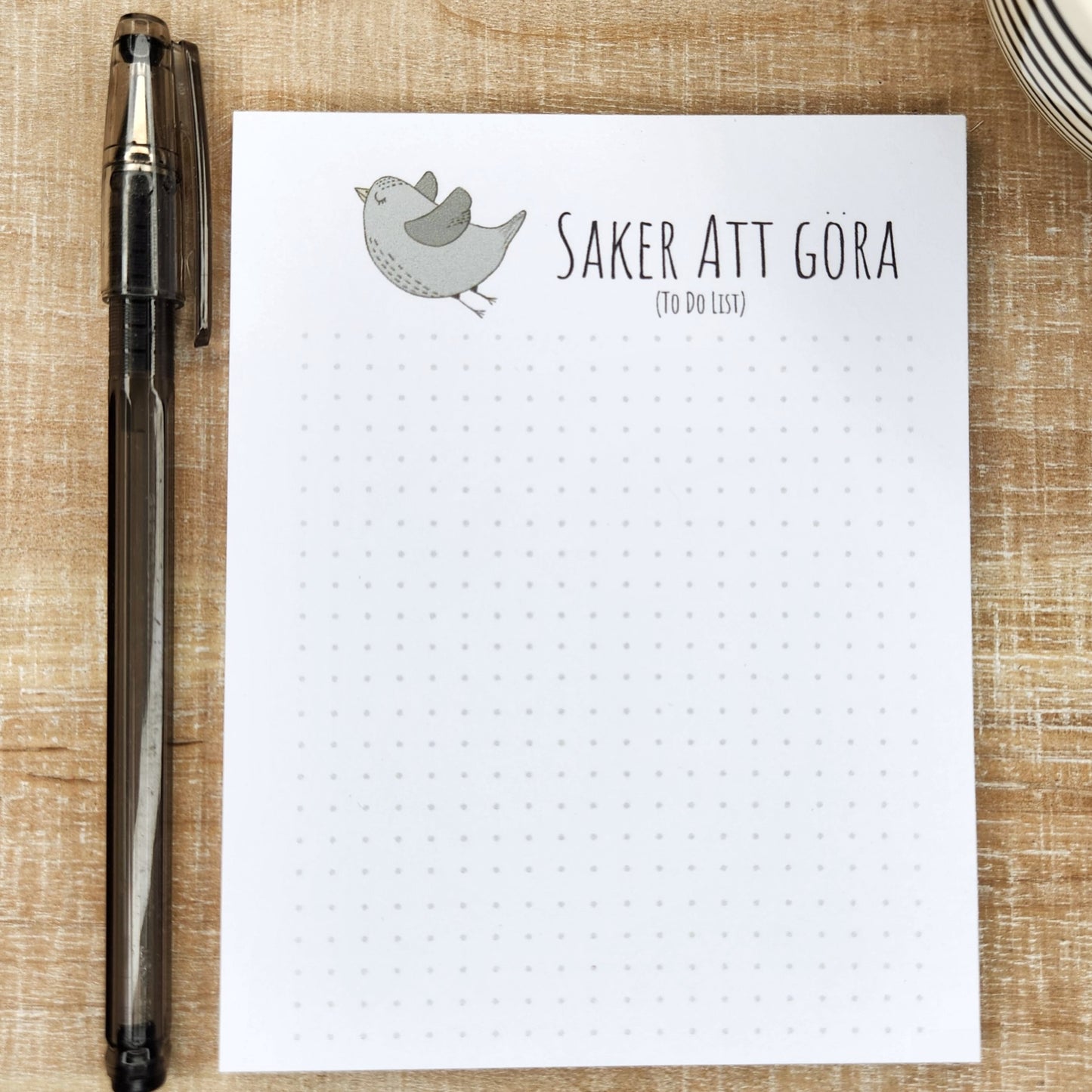 notepad on wooden background.  green/gray bird flies off to the left of the words 'saker att gora' (to do list).  A small dot grid fills out the bottom of the page.