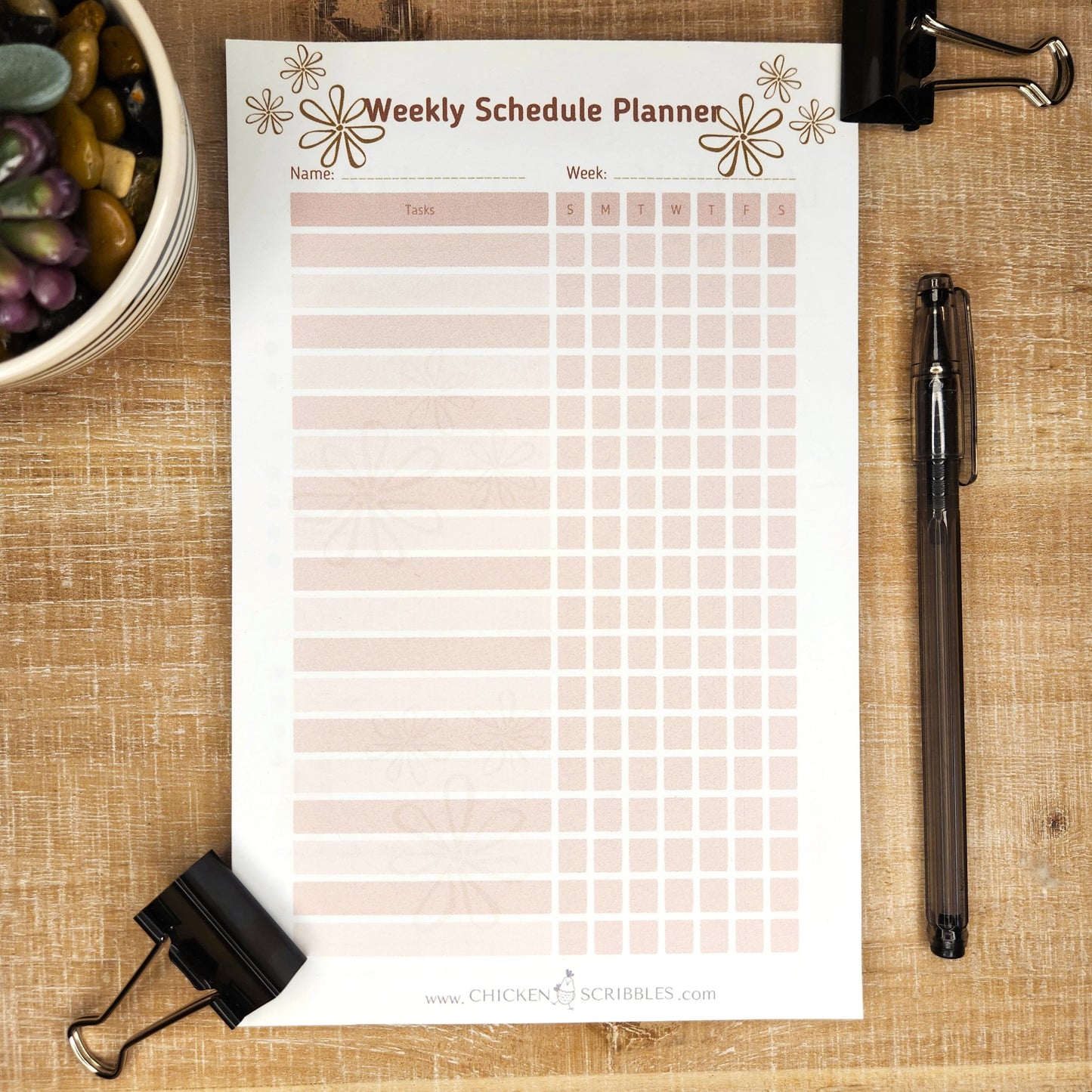 White notepad on wooden background. Notepad is a weekly schedule planner with days of the week and several lines to fill in the tasks. you can choose either tan and blue or pink and blush as the document colors.